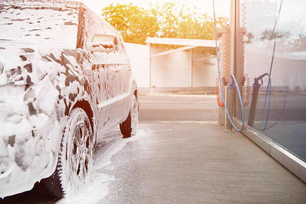 car in white cleaning foam at car wash during sunset