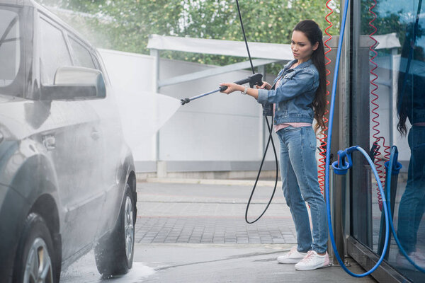 beautiful woman cleaning car at car wash with high pressure water jet