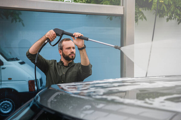 handsome man cleaning car at car wash with high pressure water jet