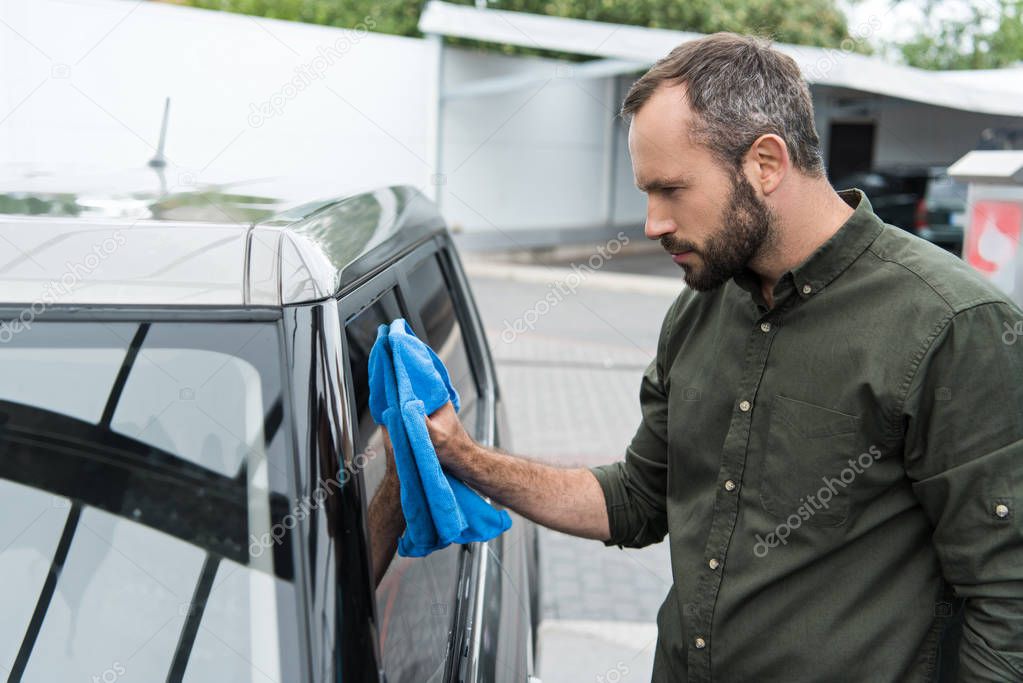 side view of handsome man cleaning car window at car wash with rag 