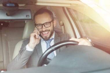 yakışıklı işadamı sürüş araba gülümseyen ve smartphone tarafından konuşuyor