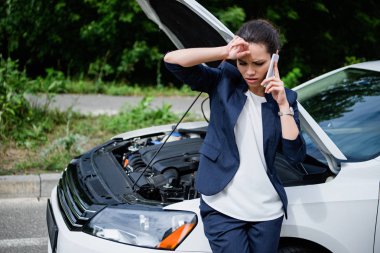 tired businesswoman talking by smartphone near broken car with open hood clipart