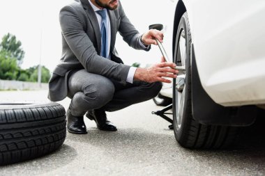 cropped image of businessman changing tires on car on road clipart