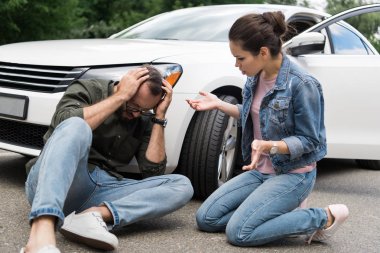 driver sitting near man on road after car accident clipart