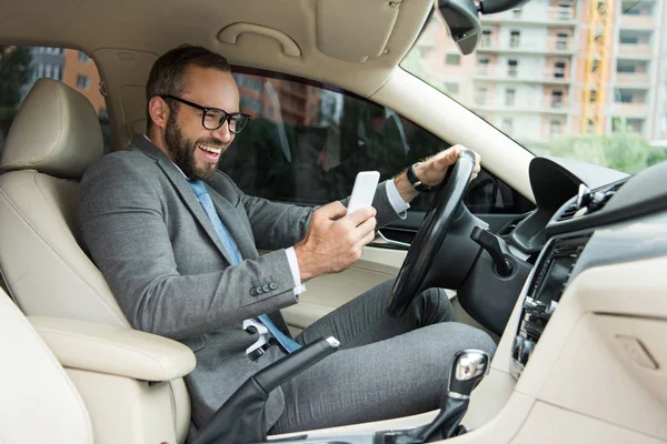 Przystojny Uśmiechnięty Mężczyzna Przy Użyciu Smartfona Podczas Jazdy Samochodem — Zdjęcie stockowe