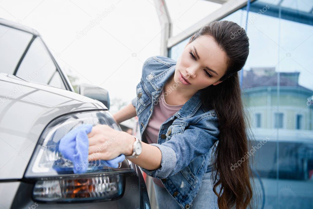 attractive woman cleaning car headlight at car wash with rag