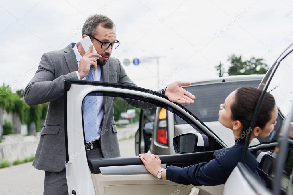 businesspeople quarreling on road after car accident, man talking by smartphone