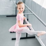 Vista de ángulo alto del niño en tutú rosa ejerciendo en la escuela de ballet