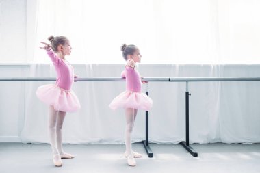 side view of beautiful little kids in pink tutu skirts practicing ballet in ballet studio clipart