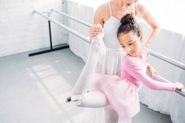 cropped shot of ballet teacher helping to stretch to cute african american child in ballet school clipart