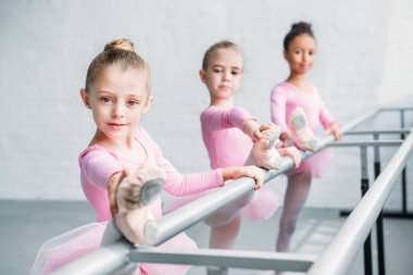 beautiful children looking at camera while stretching in ballet school clipart