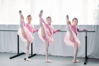 beautiful little ballet dancers exercising and looking at camera in ballet school clipart