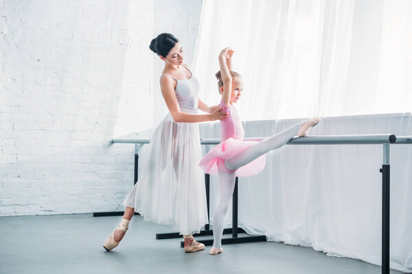 young ballet teacher exercising with cute little student in ballet studio 