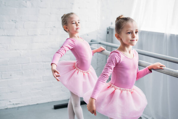 beautiful little kids in pink tutu skirts practicing ballet and looking away in ballet studio