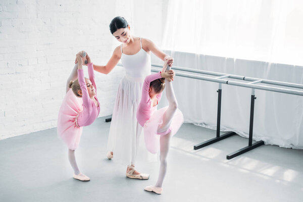 smiling young ballet teacher exercising with kids in ballet school