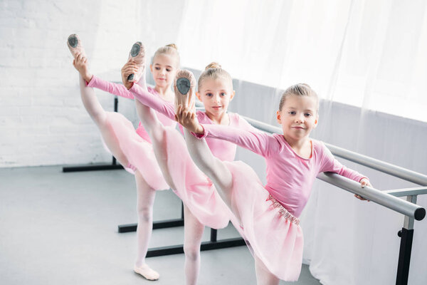 adorable kids in pink tutu skirts practicing ballet and looking at camera in ballet school