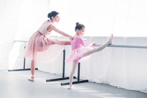 young ballet teacher looking at little student stretching in ballet studio
