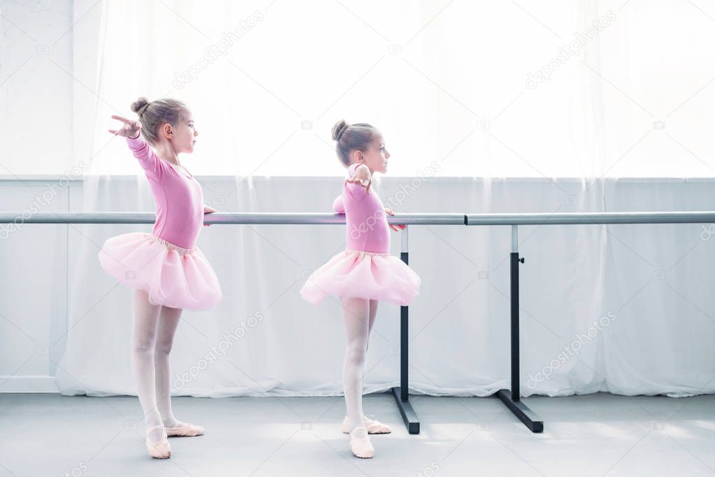 side view of beautiful little kids in pink tutu skirts practicing ballet in ballet studio