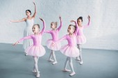 adorable kids in pink tutu skirts practicing ballet with young teacher in ballet school