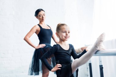 gülümseyen küçük balerin bale okulunda arkasında duran öğretmen süre germe