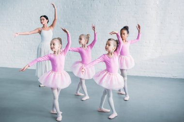 adorable kids in pink tutu skirts practicing ballet with young teacher in ballet school clipart