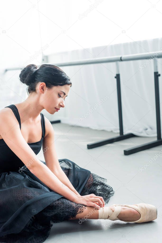 beautiful tender young ballerina sitting and tying pointe  