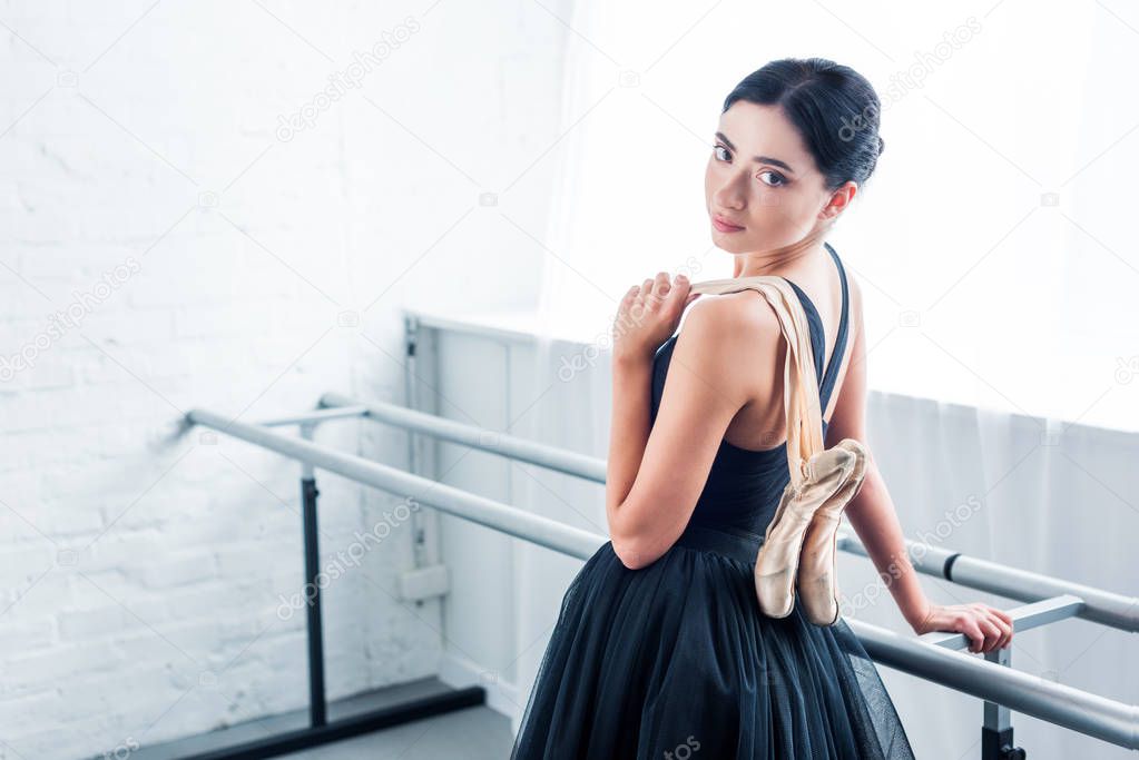 beautiful young ballerina holding pointe shoes and looking at camera