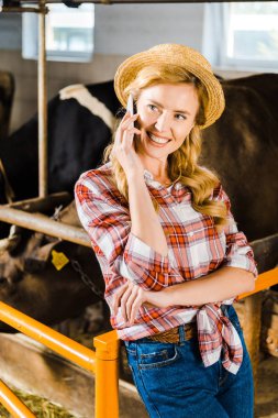 attractive smiling farmer talking by smartphone in stable clipart