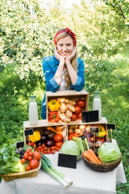 smiling farmer leaning on boxes with vegetables at farmer market clipart