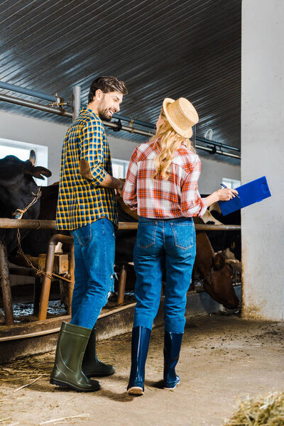 back view of couple of farmers standing in stable with clipboard