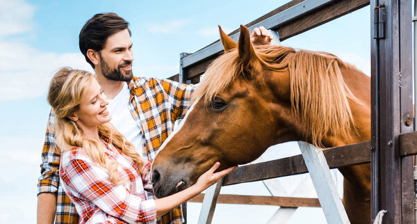 couple of smiling ranchers palming horse in stable