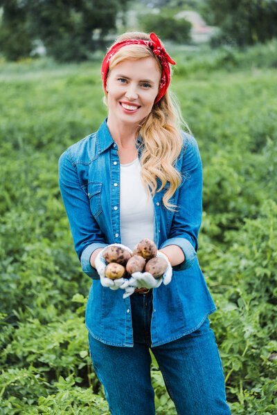 smiling attractive farmer holding ripe potatoes in field at farm