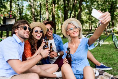 selfie yaz Park'ta dinlenme süre Smartphone'da alarak bira ile gülümseyen çok kültürlü arkadaşlar