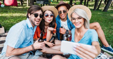 selfie yaz Park'ta dinlenme süre Smartphone'da alarak bira ile gülümseyen çok kültürlü arkadaşlar