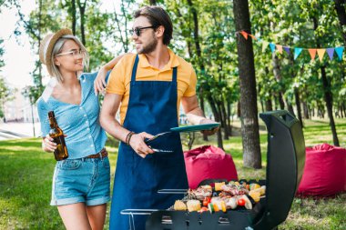 portrait of cheerful couple having barbecue in summer park clipart