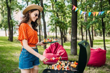 Genç kadın alarak sebze ızgara Park gülümseyen yan görünümü