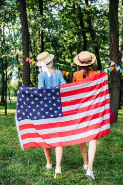 back view of friends with american flag walking in park clipart