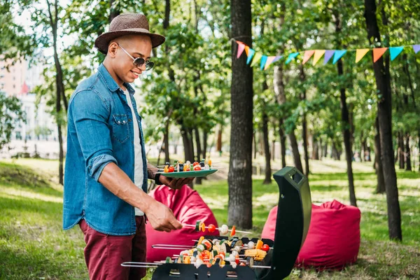 公園でバーベキュー中に野菜を焼き取って笑顔のアフリカ系アメリカ人の側面図 — ストック写真