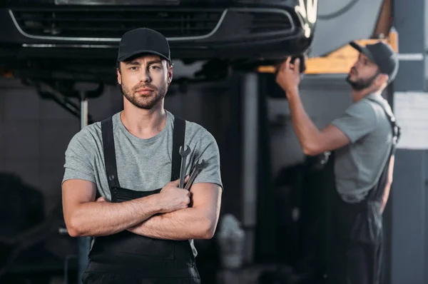 Auto Mechanic Posing Overalls Crossed Arms While Coworker Working Workshop — Stock Photo, Image