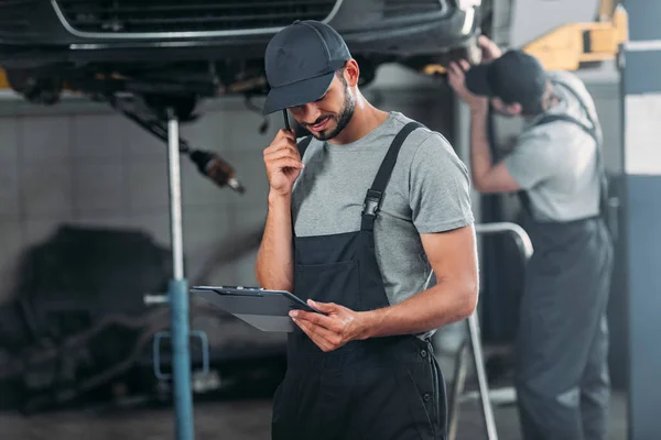 Mechanik Hovoří Smartphone Při Pohledu Schránky Zatímco Kolega Pracující Dílně — Stock fotografie