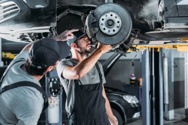 auto mechanics repairing car without wheel in workshop clipart