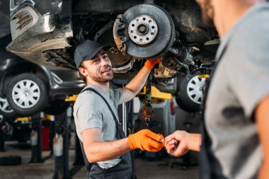 professional manual workers repairing car without wheel in mechanic shop clipart