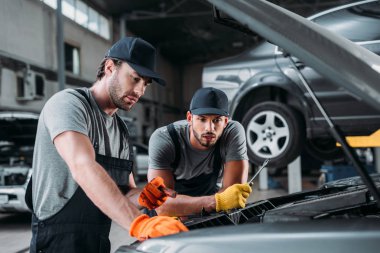 professional manual workers repairing car in mechanic shop clipart