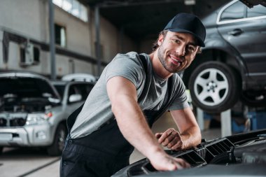 smiling auto mechanic working with car in repair shop clipart