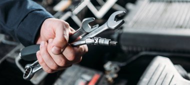 partial view of worker holding tools and wrenches in hand clipart