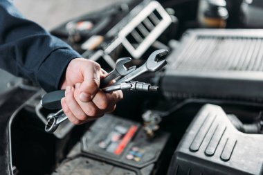cropped view of mechanic holding wrenches in hand clipart