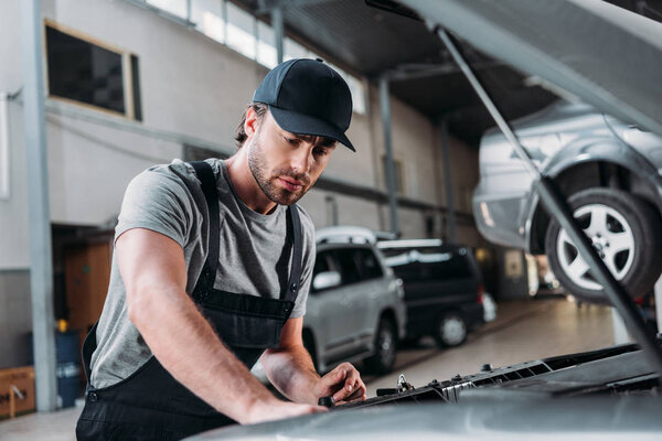 manual worker in overalls repairing car in mechanic shop