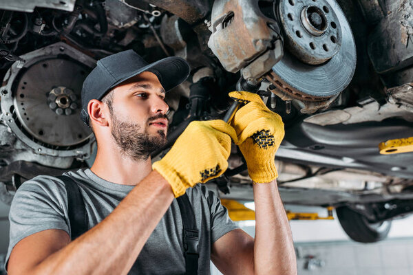 профессиональный механик в униформе ремонта автомобиля без колеса в мастерской
