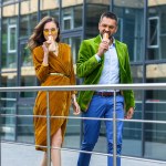 Paar im Luxus-Outfit isst französische Hot Dogs beim Gassigehen auf der Straße