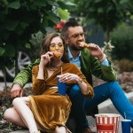 Fashionable couple in velvet clothing eating fried chicken legs on street